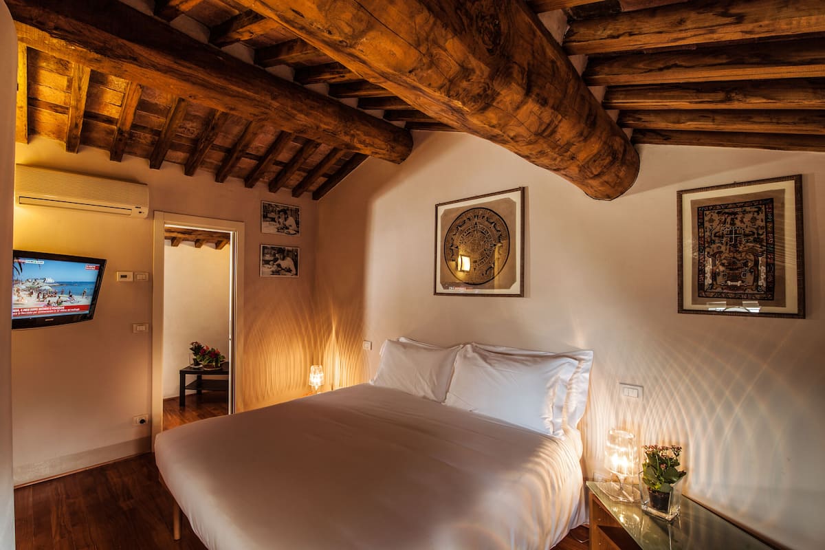A bedroom with a wooden ceiling, a bed, a wall-mounted TV, and framed artwork.