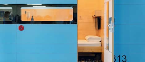 A compact hotel room with a small bed, a wooden cabinet, and a blue wall with the number 313.