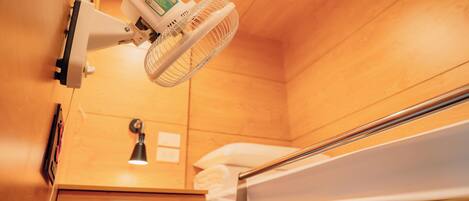 A wooden bunk bed with a bedside table and lamp, a wall-mounted fan, and a wooden wall panel.
