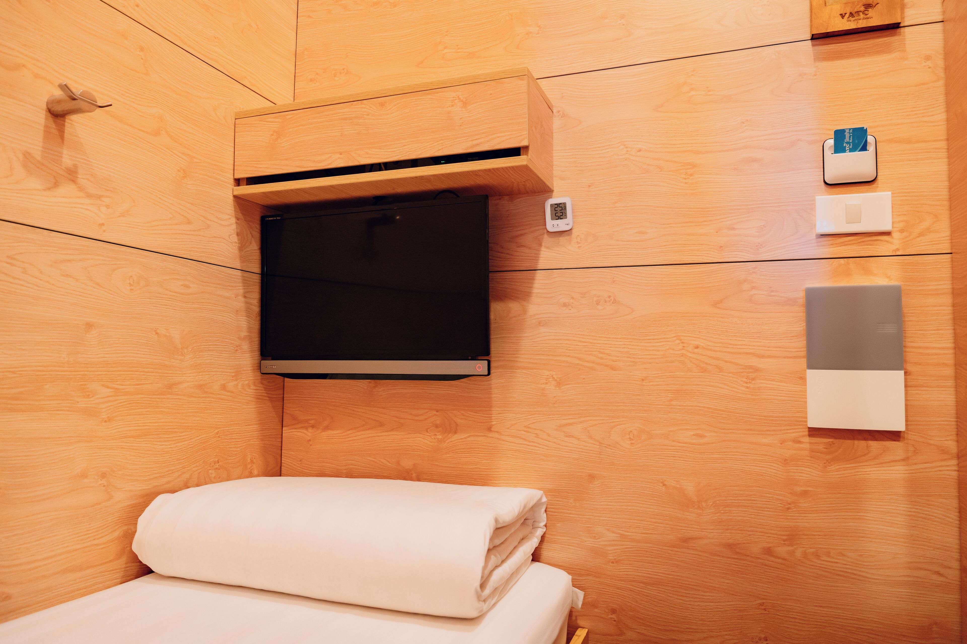 Una habitación con paneles de madera, una cama, un televisor montado en la pared, un termostato y una estación de carga.