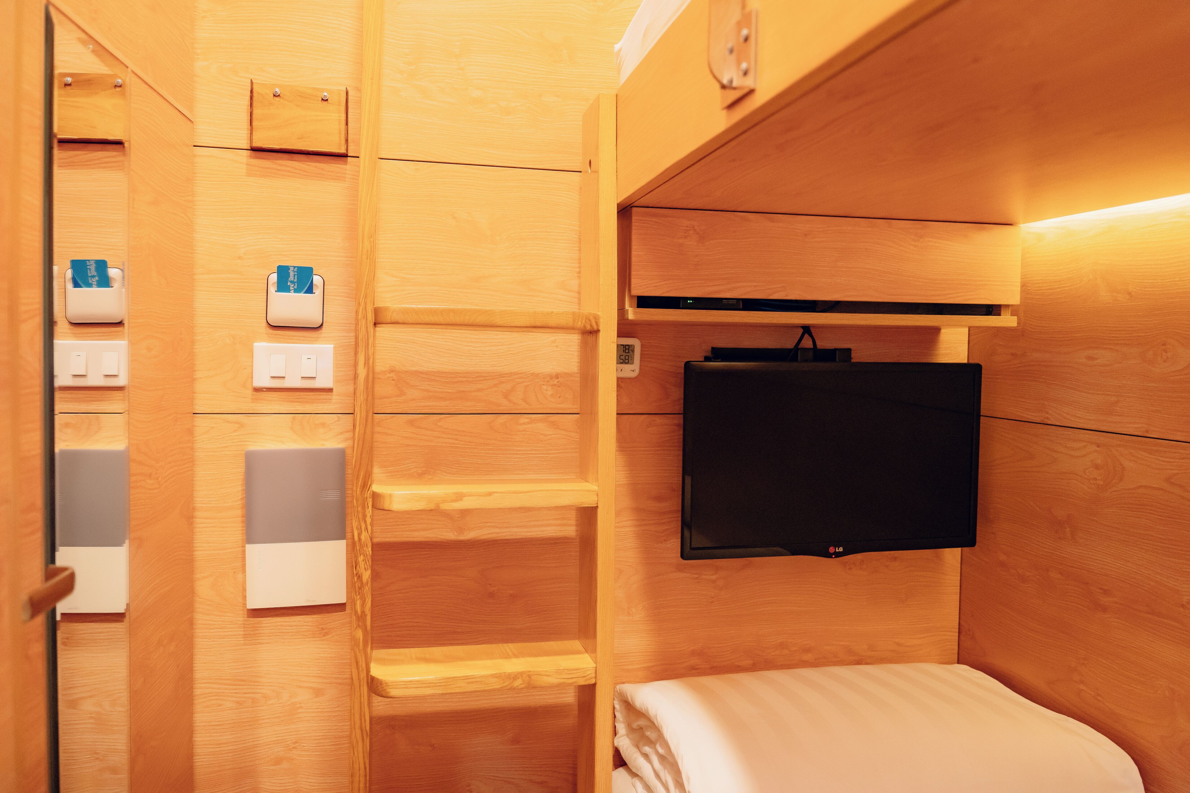 A compact room with a bed, a mounted TV, and a wooden wall with built-in storage.