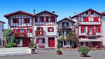 A row of traditional half-timbered buildings with red and white facades, balconies with flowers, and outdoor seating areas.