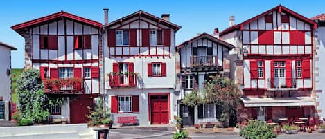 Una hilera de edificios tradicionales con entramado de madera y fachadas rojas y blancas, balcones adornados con flores y terrazas al aire libre.