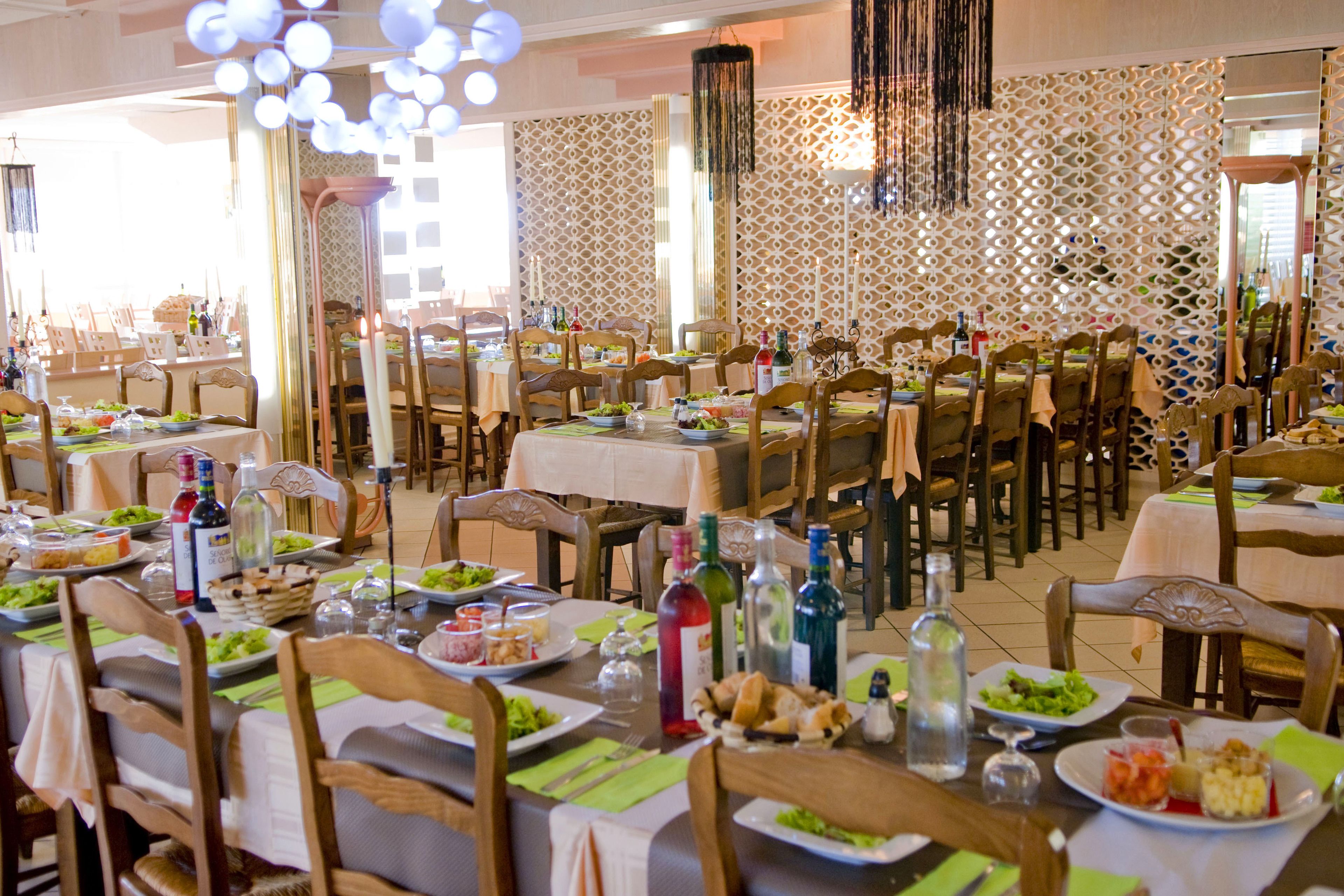 A dining area with multiple tables set for meals, each with plates of food, cutlery, and bottles.
