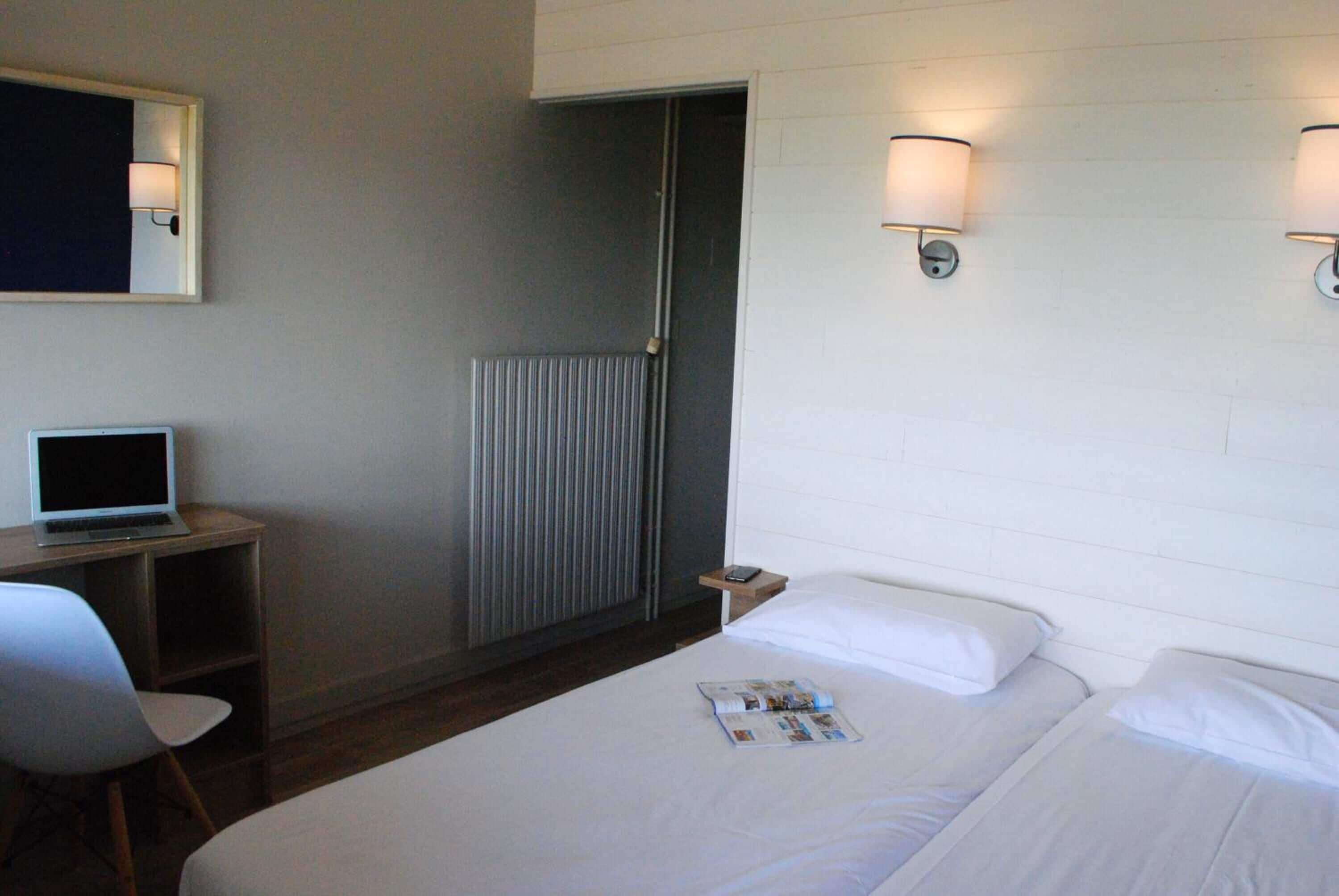 Een hotelkamer met een bed, een bureau met een laptop, een stoel en een deur naar een badkamer.