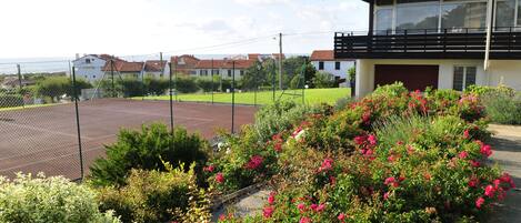 A residential area with a tennis court, a house with a balcony, and a garden with flowering plants.
