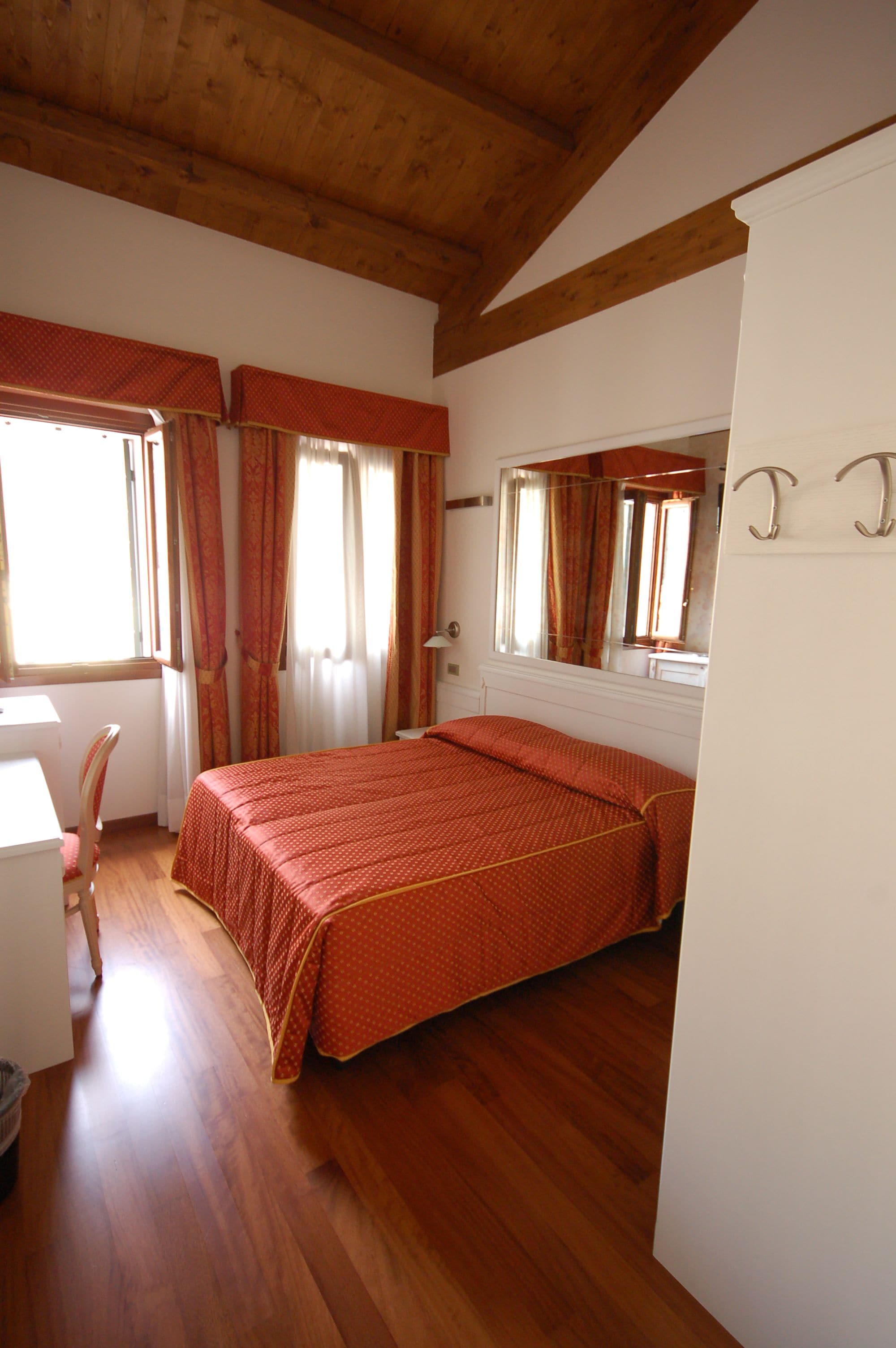 Ein Schlafzimmer mit Holzboden, einem Bett mit roter Bettdecke, einem Schreibtisch und einem Stuhl.