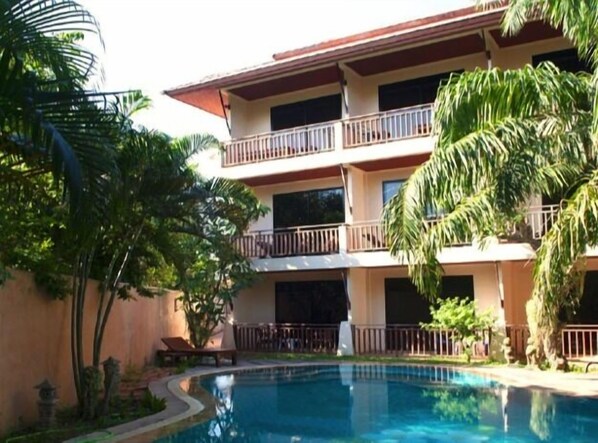 A multi-story hotel with a swimming pool, surrounded by tropical vegetation.