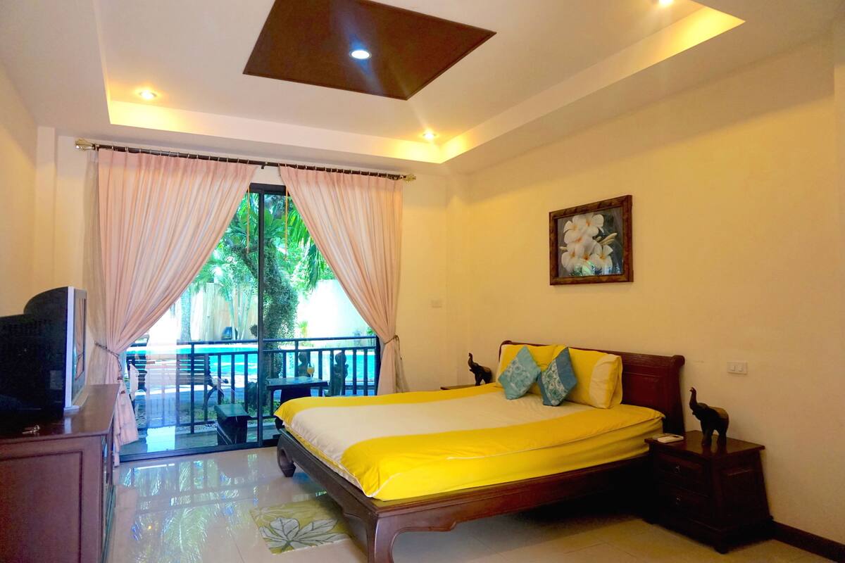 Quarto de hotel com cama, mesa de cabeceira, televisão e varanda com vista para vegetação.