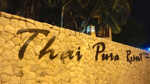 Un muro de piedra con el texto "Thai Pua Resort" iluminado en negro.