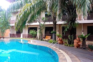 A swimming pool with a curved edge, surrounded by a wooden deck and palm trees.