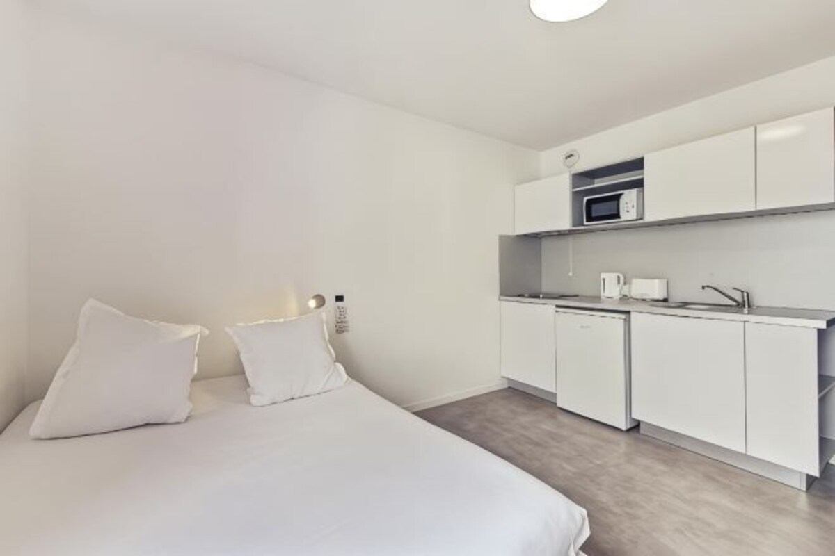 Ein Zimmer mit einem Bett, einer Küchenzeile und einer weißen Farbgestaltung.