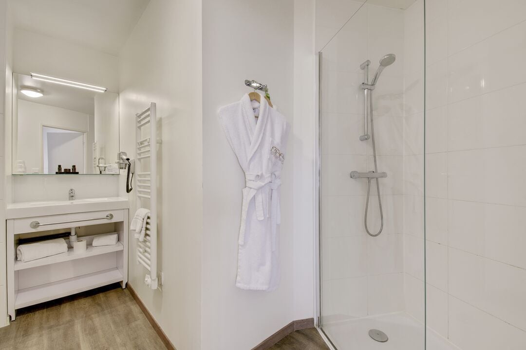 Un baño moderno con cabina de ducha de vidrio, tocador blanco con espejo y una bata colgada en la pared.