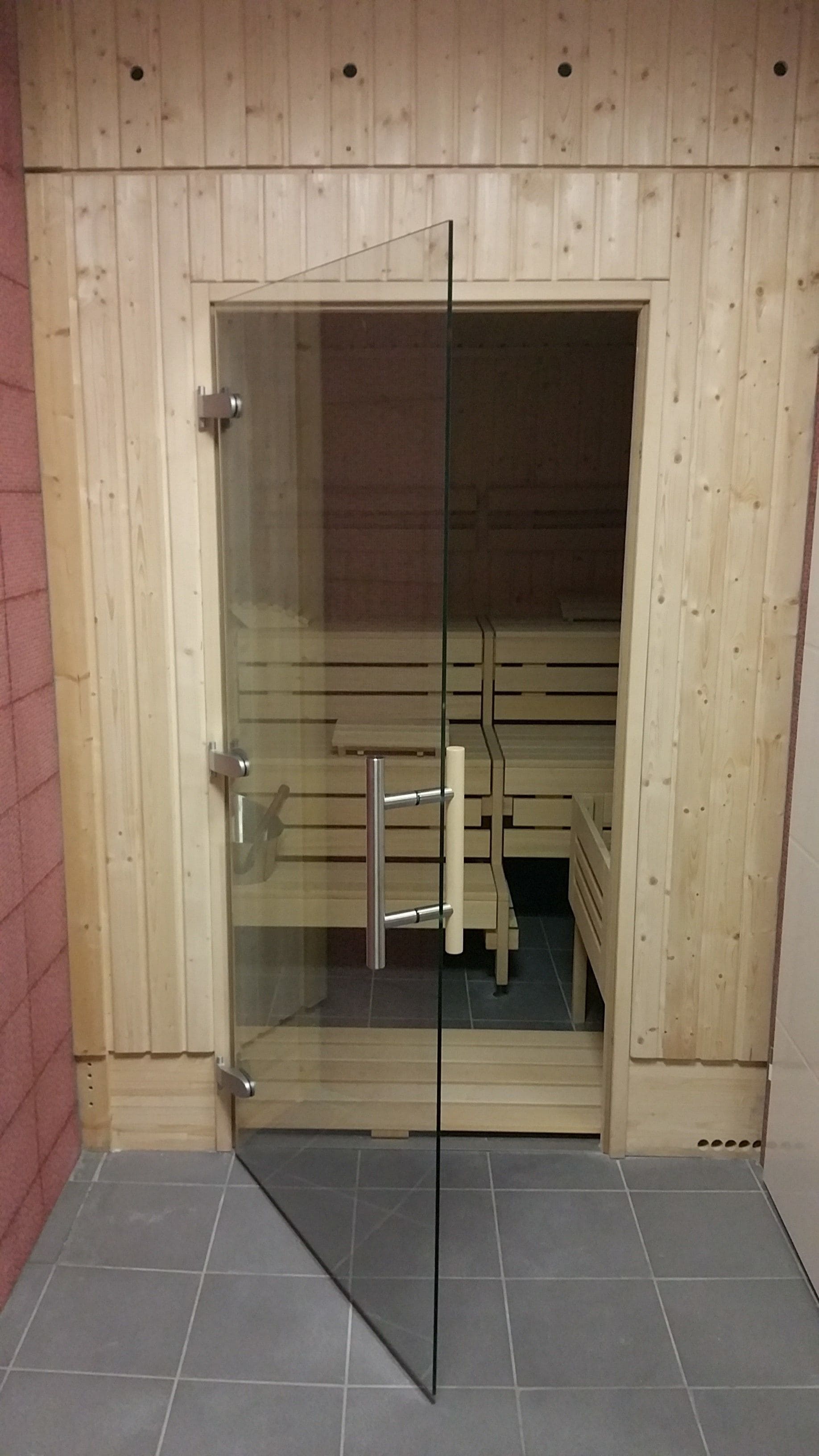 A wooden sauna with a glass door, a metal railing, and a bench inside.