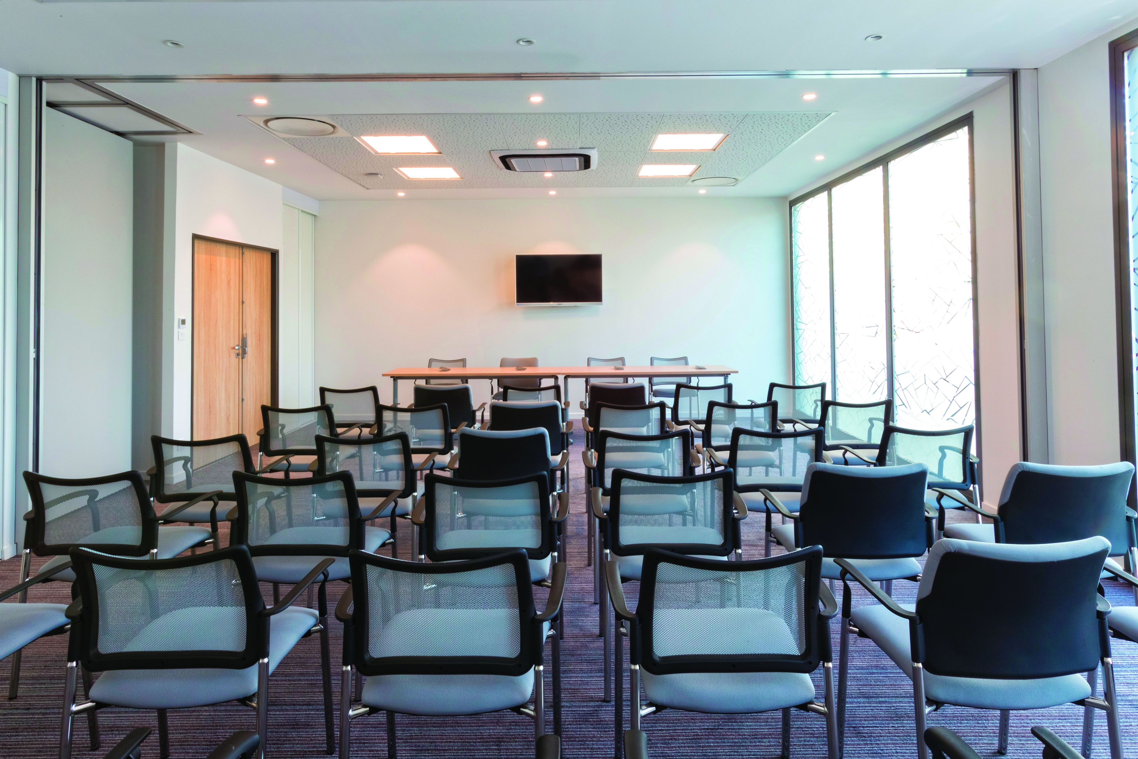 A conference room with rows of chairs, a large table, and a television screen.