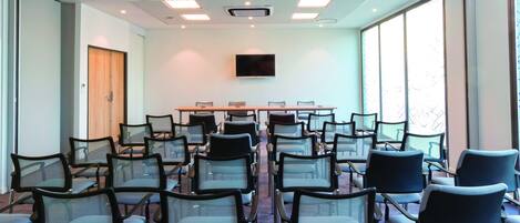 A conference room with rows of chairs, a large table, and a television screen.