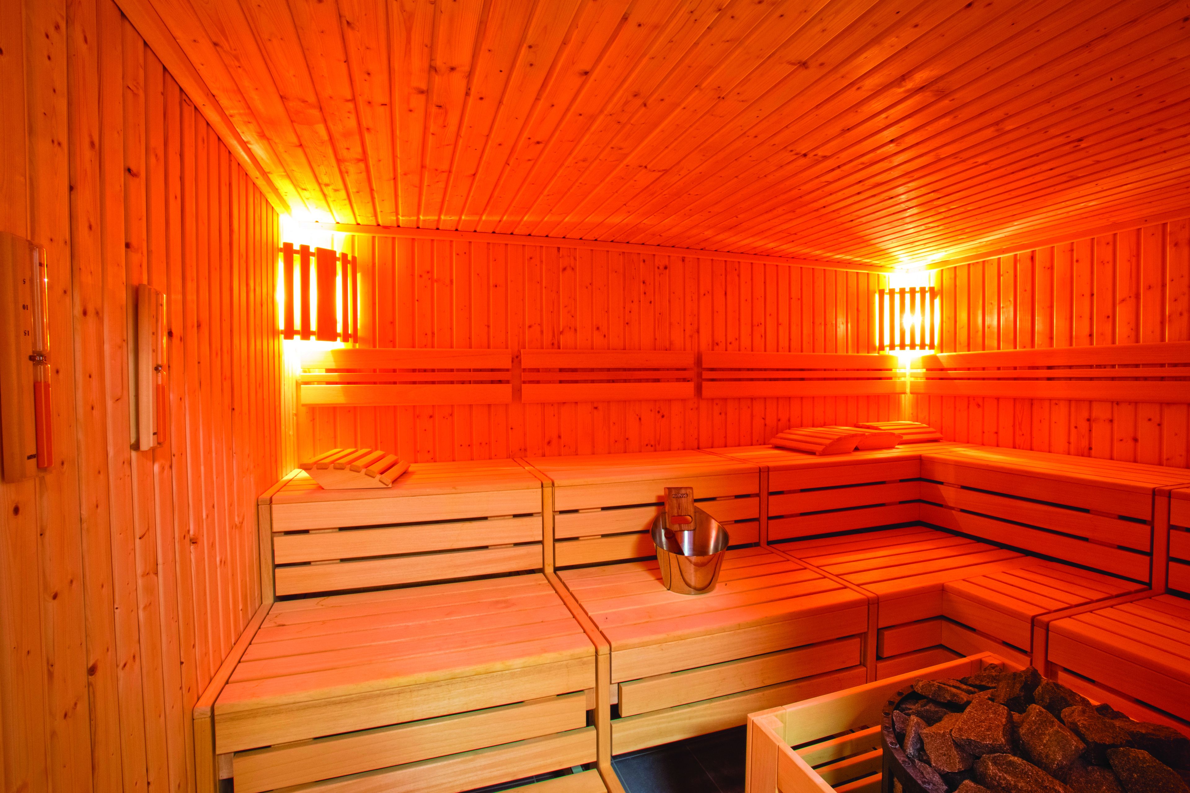 Una sauna con bancos de madera, un recipiente metálico y un banco de piedra.
