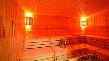 Una sauna con bancos de madera, un recipiente metálico y un banco de piedra.