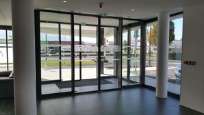 Ein moderner Hotel-Eingang mit Glasüren, freier Sicht auf die Straße und Hinweisschildern.