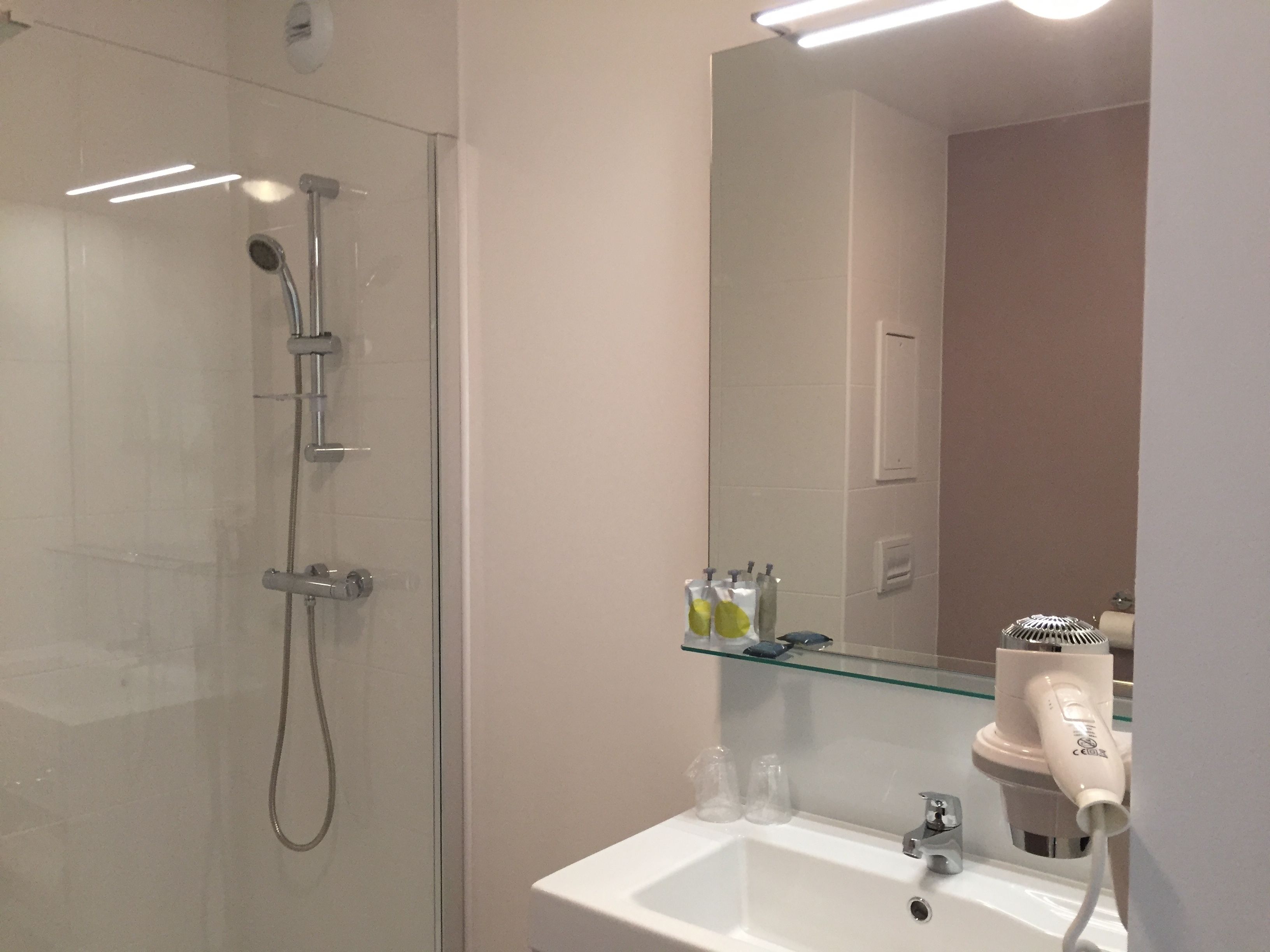 A bathroom with a glass-enclosed shower, a white sink, a mirror, and a hairdryer on a shelf.