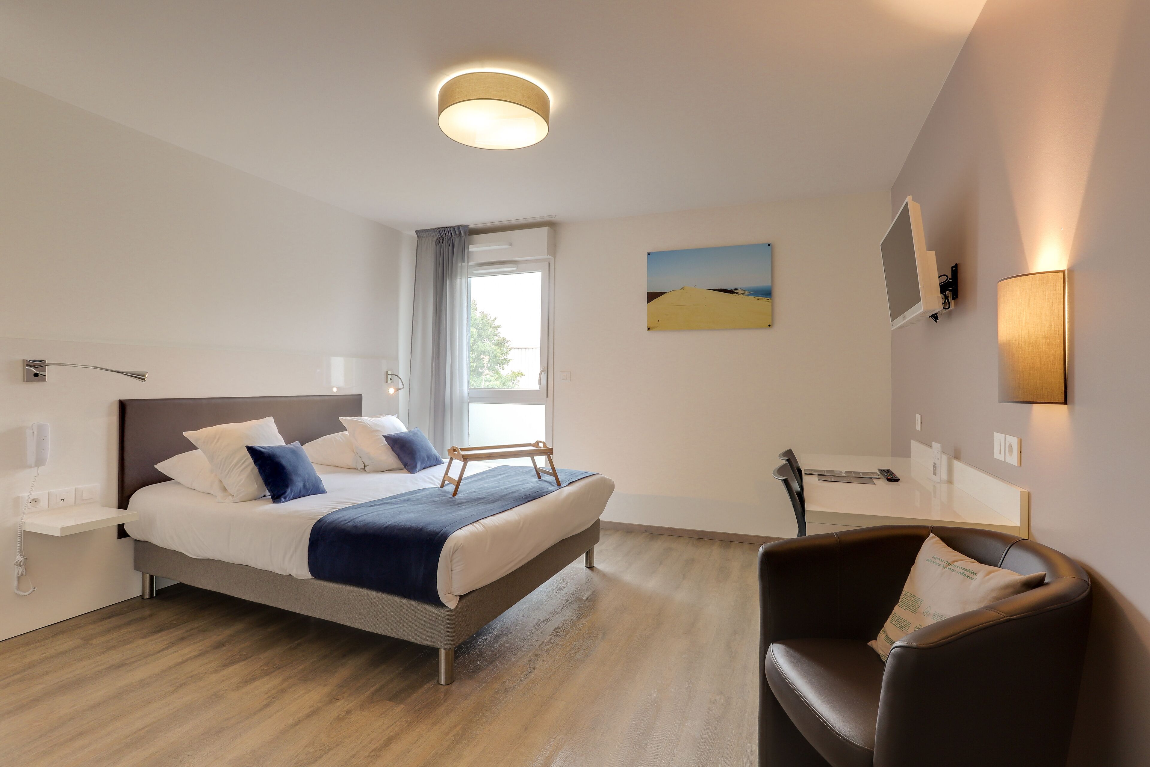 Una habitación de hotel moderna con una cama, un escritorio, una silla y un ventanal.