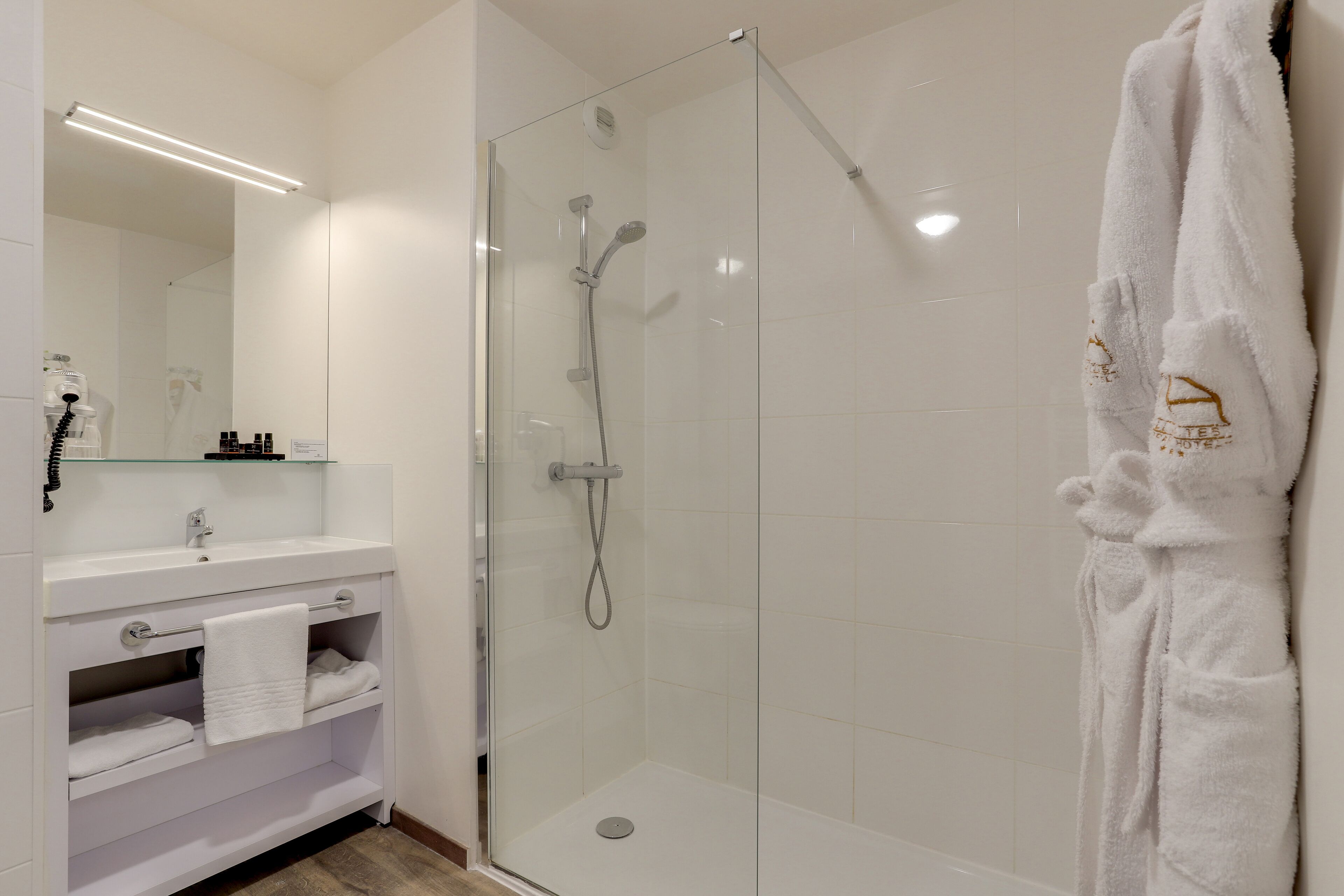 Een moderne badkamer met een glazen douchecabine, een wit wastafelmeubel met handdoekhouder en een badjas aan de muur.