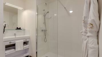 Een moderne badkamer met een glazen douchecabine, een wit wastafelmeubel met handdoekhouder en een badjas aan de muur.