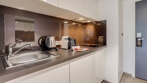 Eine moderne Küche mit Spüle aus Edelstahl, einem Wasserkocher und einem Toaster. Über der Spüle hängt ein Spiegel, und eine Tür trägt ein Schild.