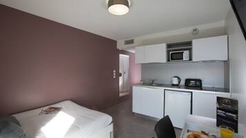 Een compacte hotelkamer met een bed, een kleine kitchenette en een eethoek.