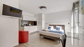 Ein modernes Hotelzimmer mit einem Bett, einem roten Hocker, einer Küchenzeile und einem an der Wand befestigten Fernseher.