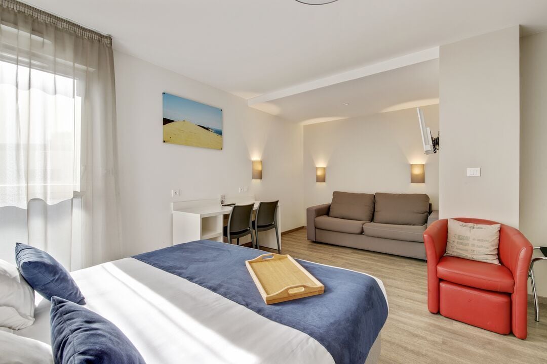 A hotel room with a bed, a desk, a sofa, and a red chair.