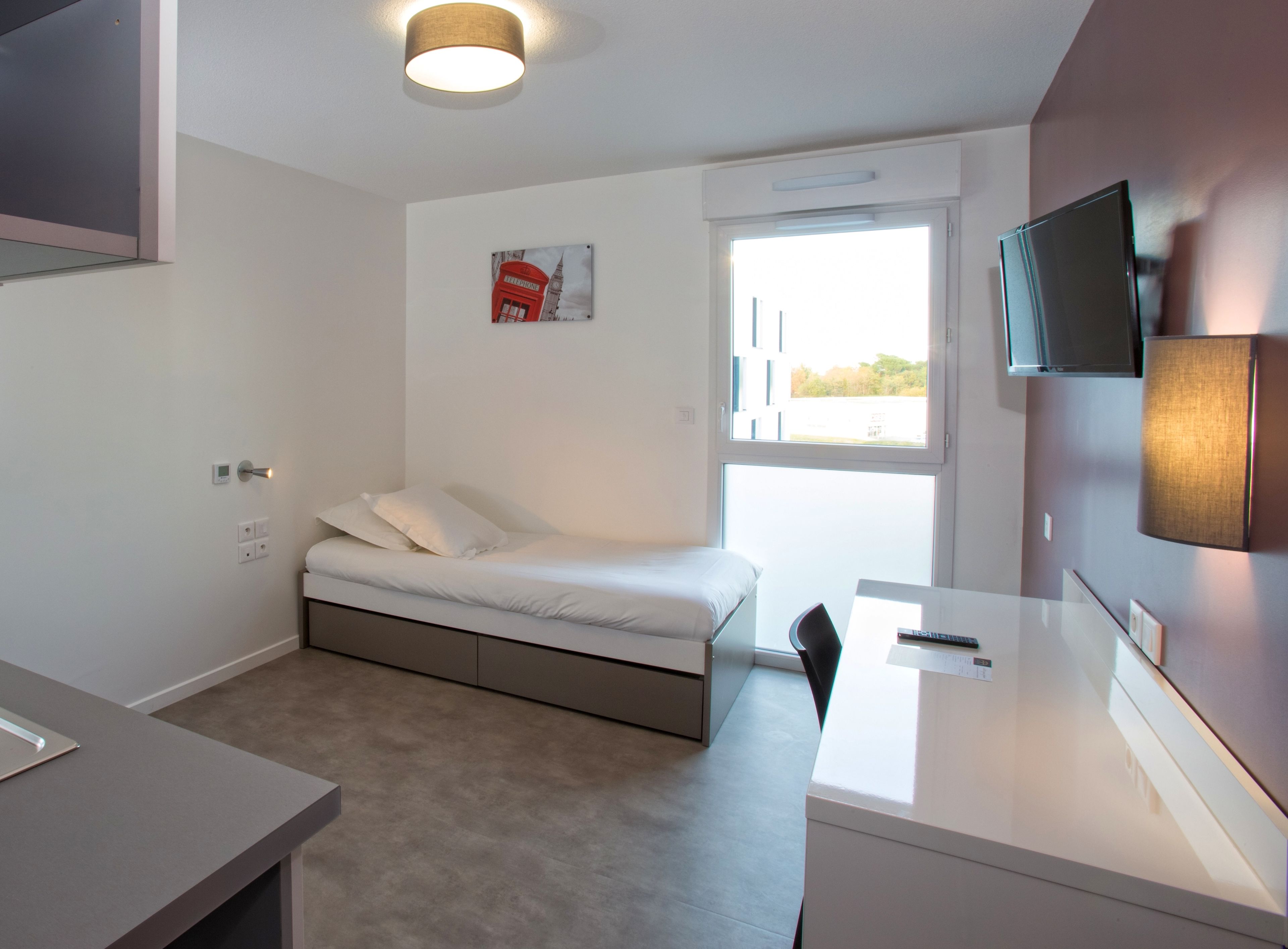 Un dormitorio moderno con cama, escritorio, silla, televisor y ventana.