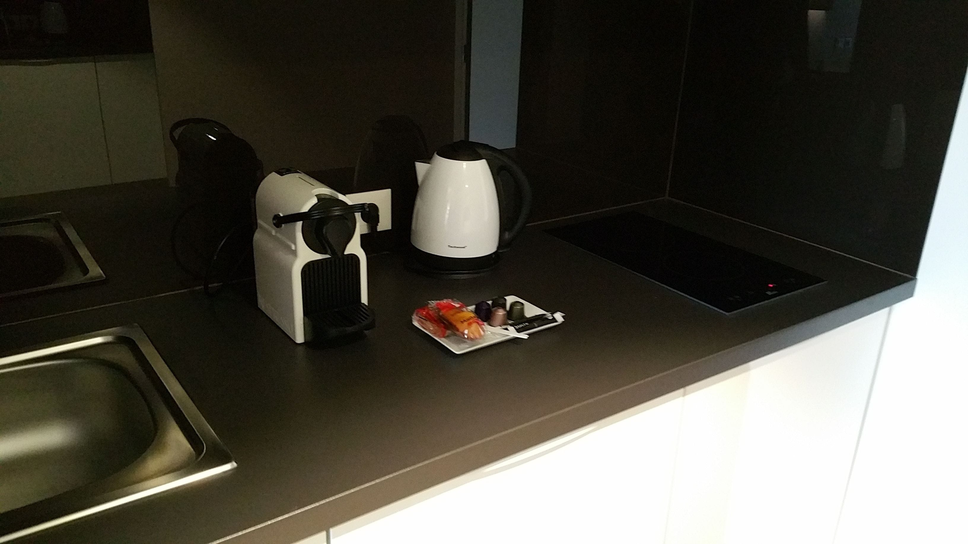 A modern kitchen with a coffee maker, kettle, and a small plate with a wrapped item.