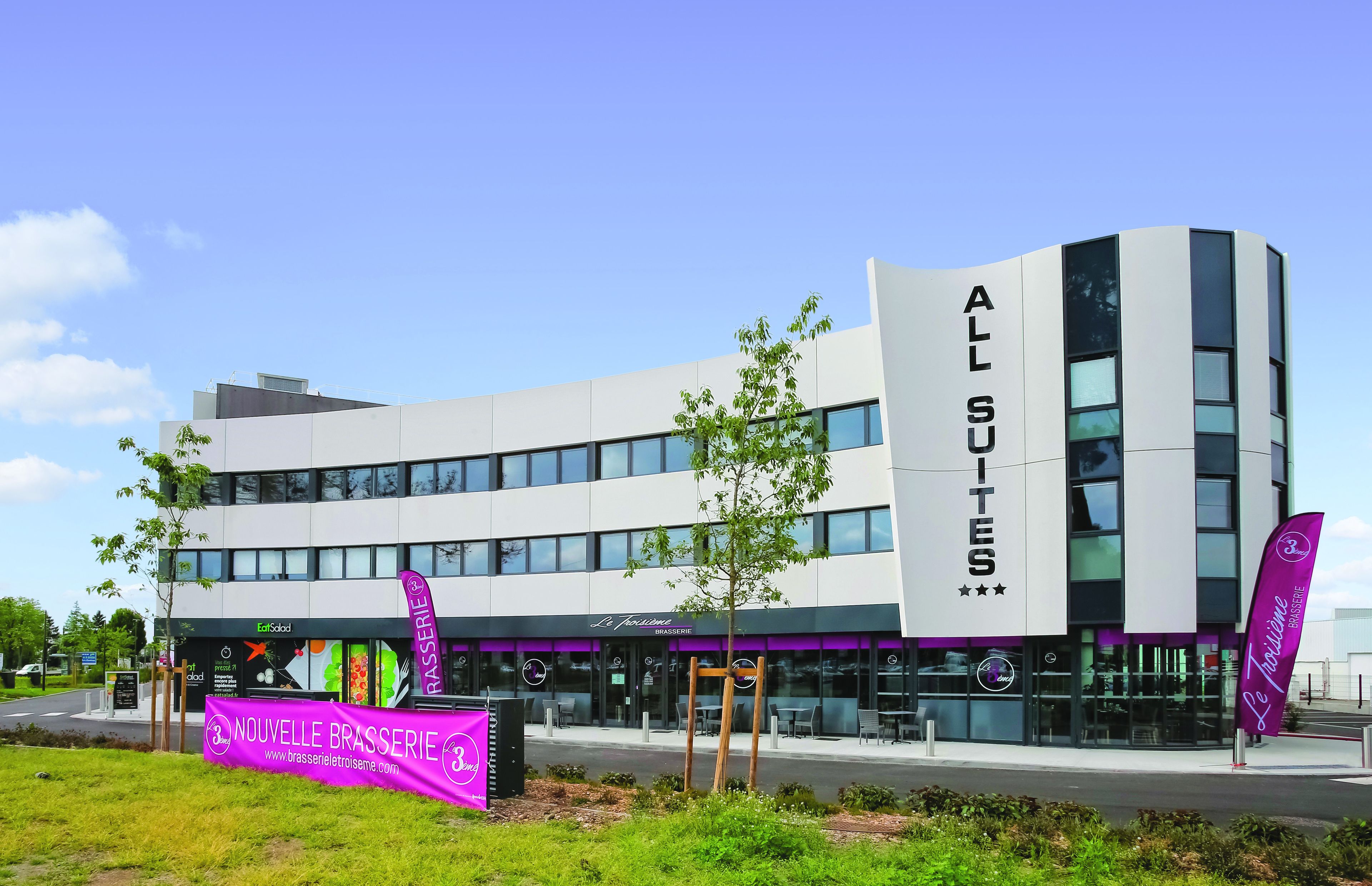 A modern hotel with a curved facade, multiple windows, and a prominent sign for 'ALL SUITES'.