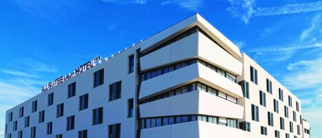 A multi-story hotel with a flat facade, numerous windows, and a sign reading "ALL QUINTS APART HOTEL".