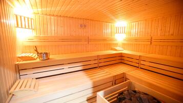 A sauna with wooden benches and benches, a metal bucket, and a heater.
