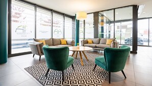 Eine moderne Lobby mit einer Sofagarnitur, zwei Sesseln, einem runden Tisch und einem gemusterten Teppich.