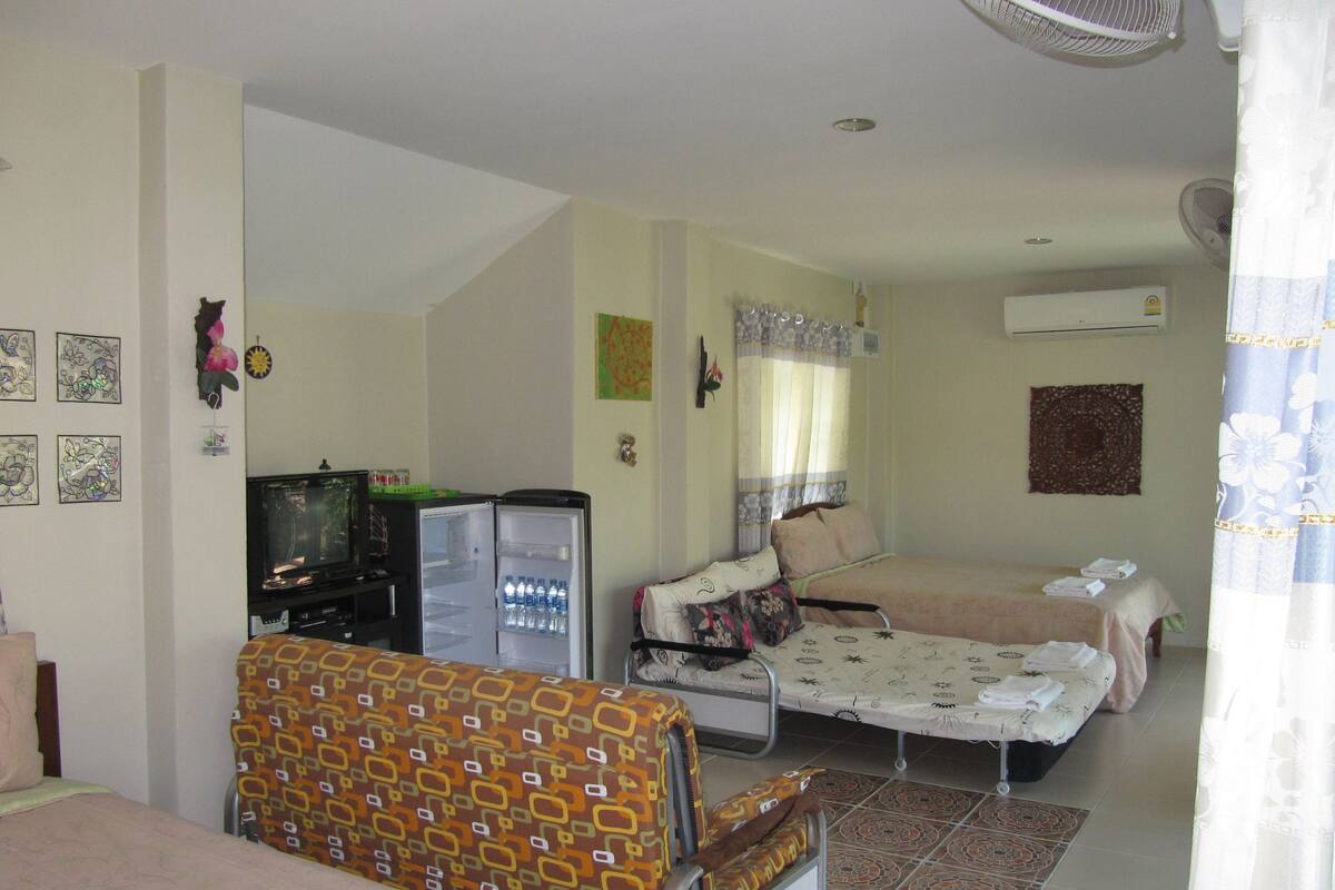 A compact hotel room with a bed, a small seating area, a refrigerator, and a television.