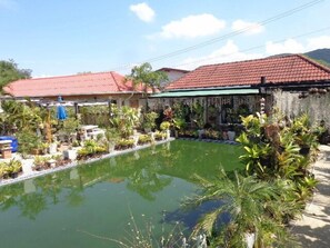 Une piscine entourée de plantes en pot et un bâtiment avec un toit rouge.