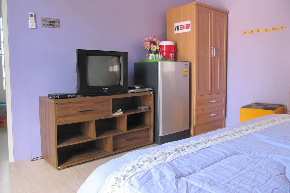 A bedroom with a bed, a television, a refrigerator, and a wooden cabinet.