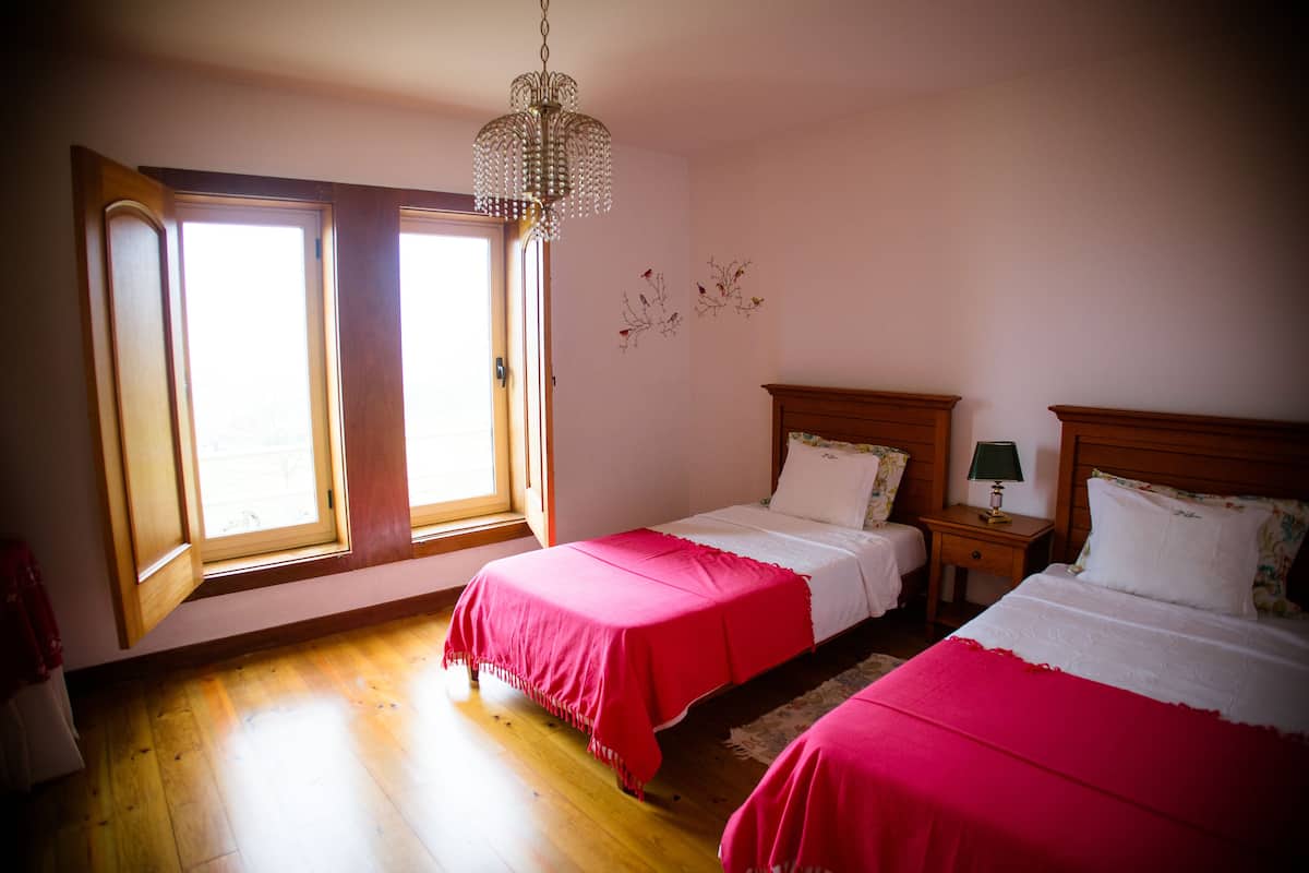Un dormitorio con dos camas, suelo de madera, un candelabro y una ventana con persianas.