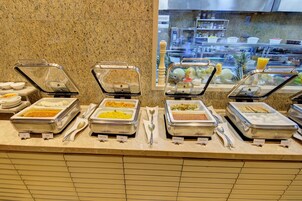 Un bufé con distintos alimentos en recipientes transparentes, una cuchara y una servilleta sobre el mostrador.