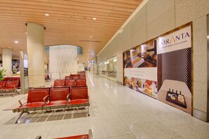 A spacious airport transit hotel corridor with red seating, a wooden ceiling, and a large advertisement for Niranta. - Niranta Airport Transit Hotel & Lounge Terminal 2 Arrivals (Mumbai)