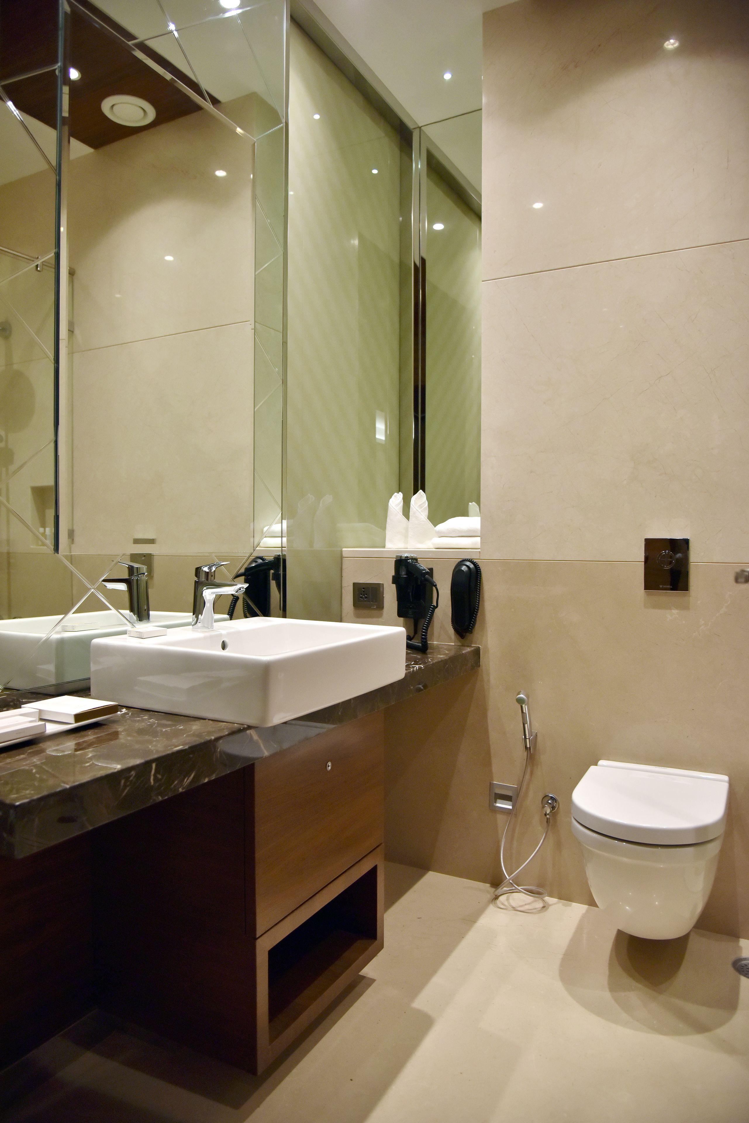 A modern bathroom with a large mirror, two sinks, a toilet, and a shower.