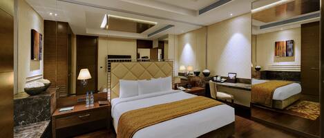 A hotel room with a large bed, a desk, a chair, a mirror, and a bathroom.