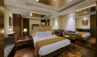 A hotel room with a large bed, a desk, a chair, a mirror, and a bathroom.