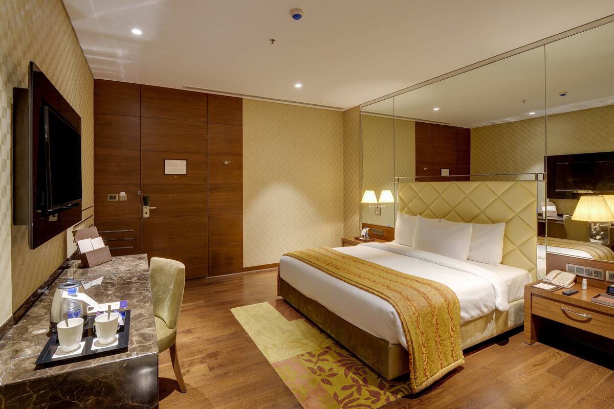 Ein Hotelzimmer mit Bett, Nachttisch, Lampe, Fernseher und Schreibtisch mit Kaffeemaschine und Tassen.