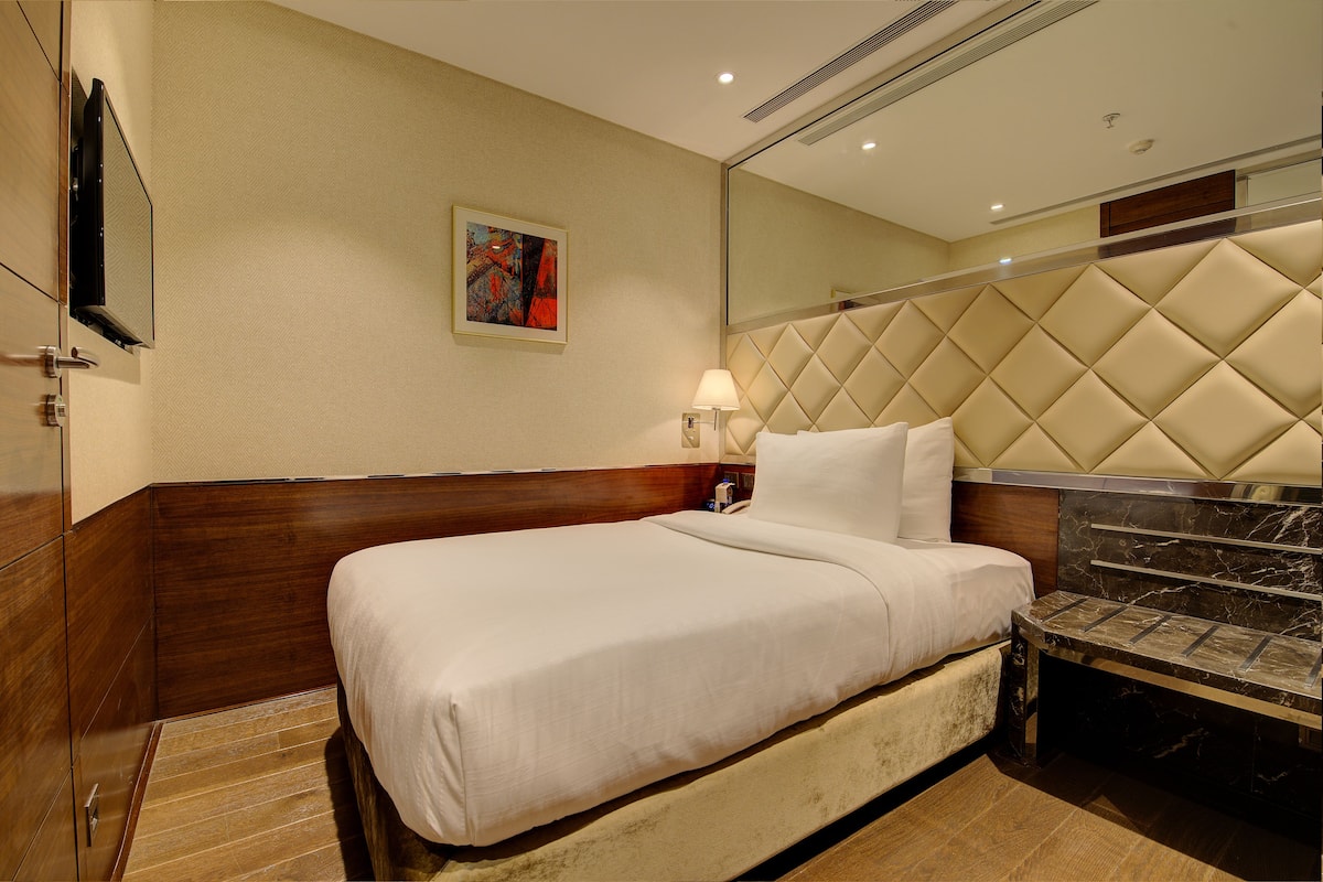 Ein Hotelzimmer mit einem großen Bett, einem Kopfteil mit Rautenmuster, einem Nachttisch mit Lampe und einem großen Spiegel über dem Bett.