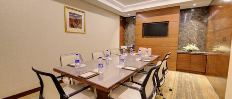 A conference room with a long table, chairs, water bottles, and a TV on the wall.