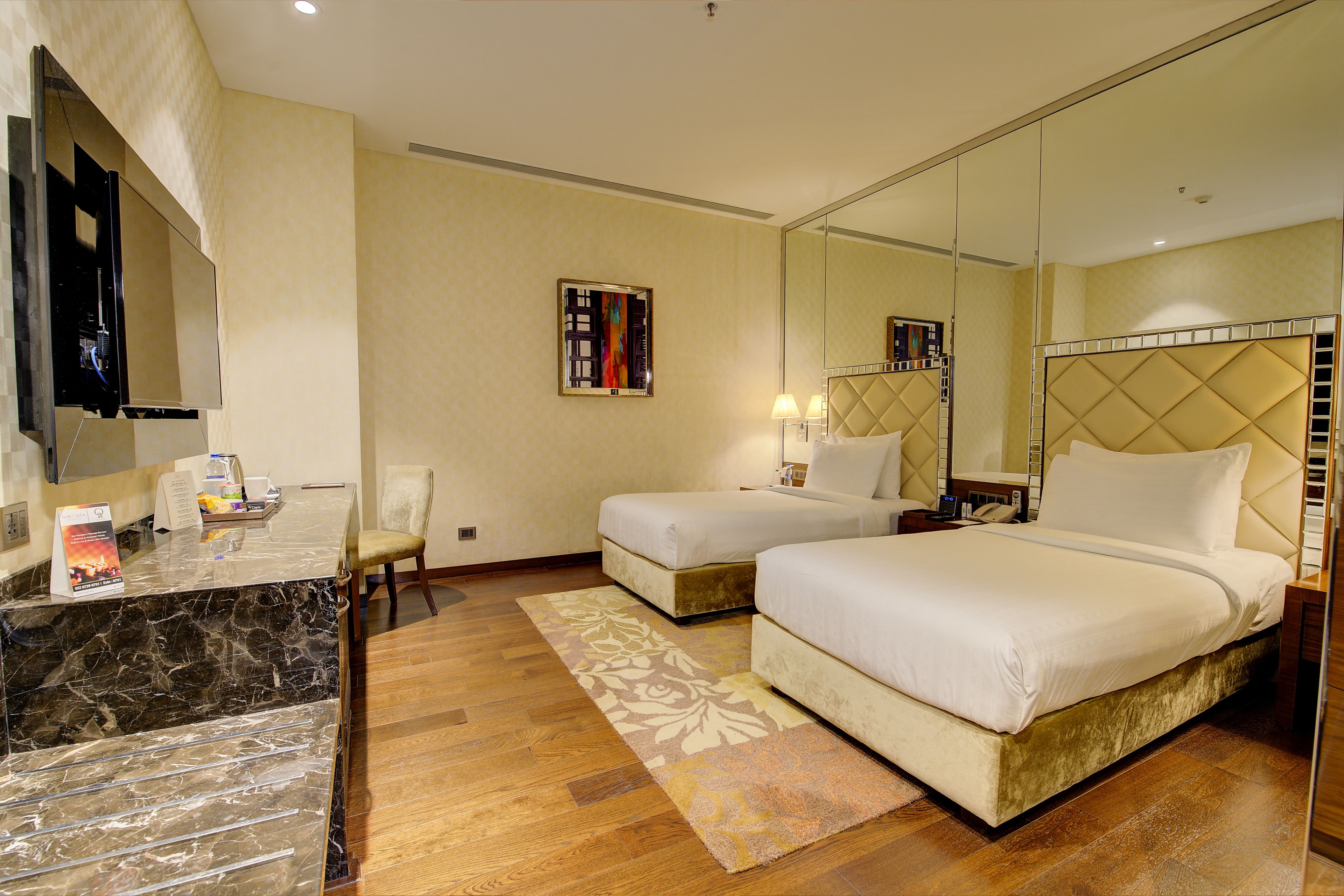 A hotel room with a marble reception desk, two beds with headboards, a large mirror, and a wooden floor.